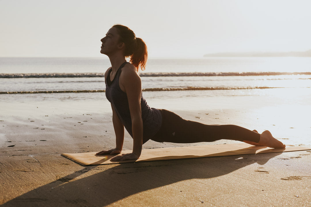 Yogi in upward dog on yoga mat on NZ beach