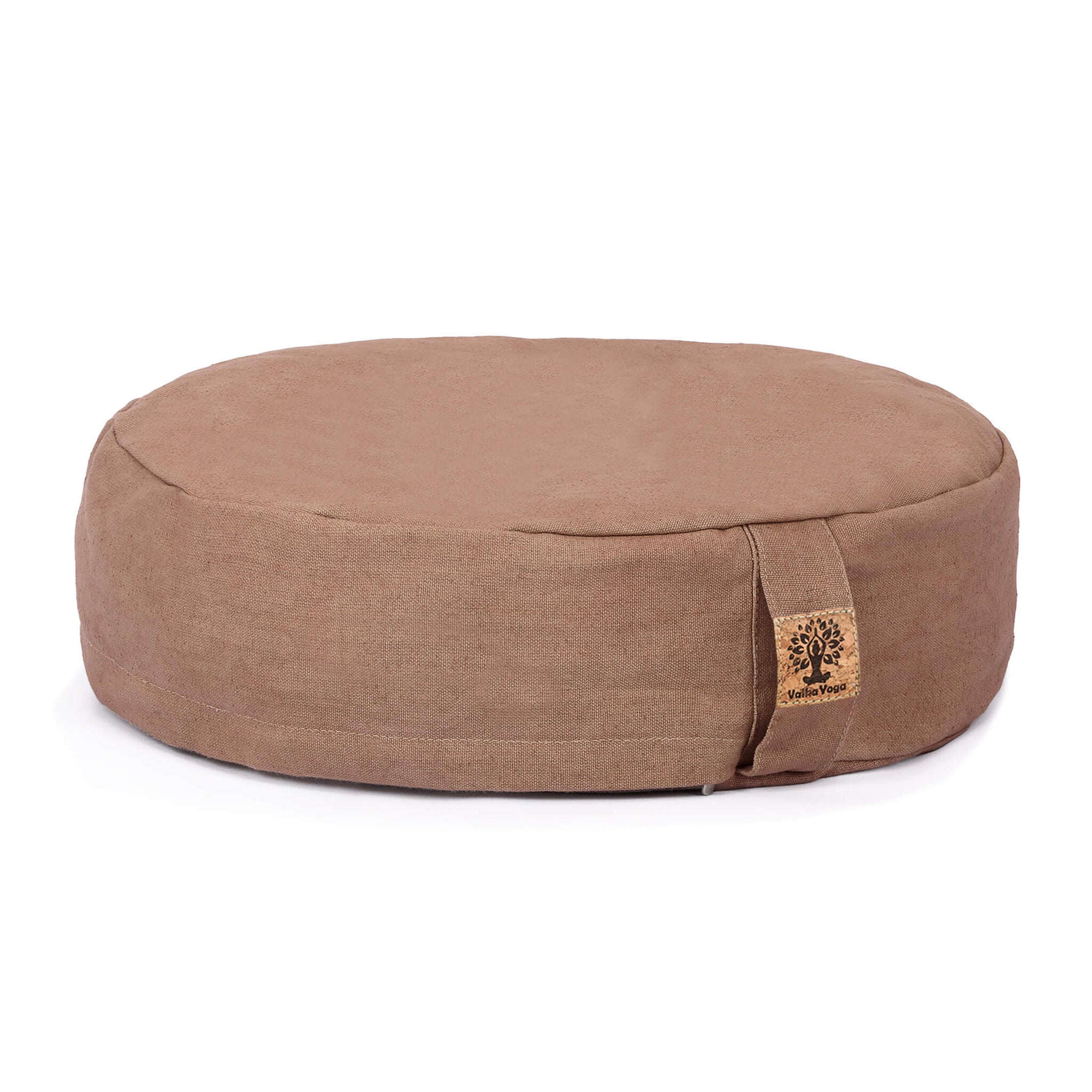 A round meditation cushion in a warm taupe-brown fabric, featuring a small sewn-on cork patch on the front right side, set against a plain white background