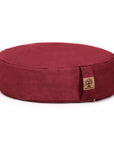 A round, deep red fabric meditation cushion with a small cork tag on the side, photographed on a clean white background