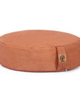 A round, earth-toned pink cushion with a small fabric brand tag on the side, photographed on a clean white background