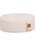 A round, off-white fabric meditation cushion with a small cork logo patch on the side, photographed against a solid white background