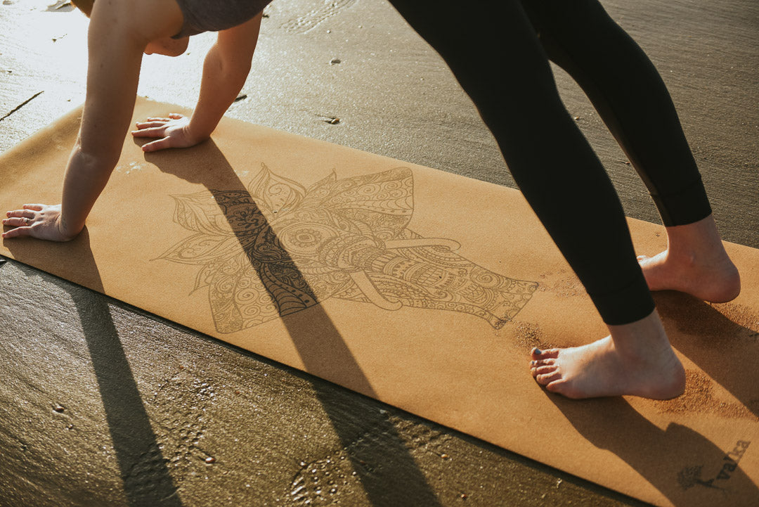 Yogini in downward dog on yoga mat on NZ beach